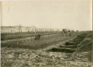 An American cemetery north of Toul, France 1918. Wooden crosses are grave markers, on the freshly-dug graves, with filled-in graves on the left. In the center are Troops completing the burials. Henry L. Graves. State Archives of North Carolina